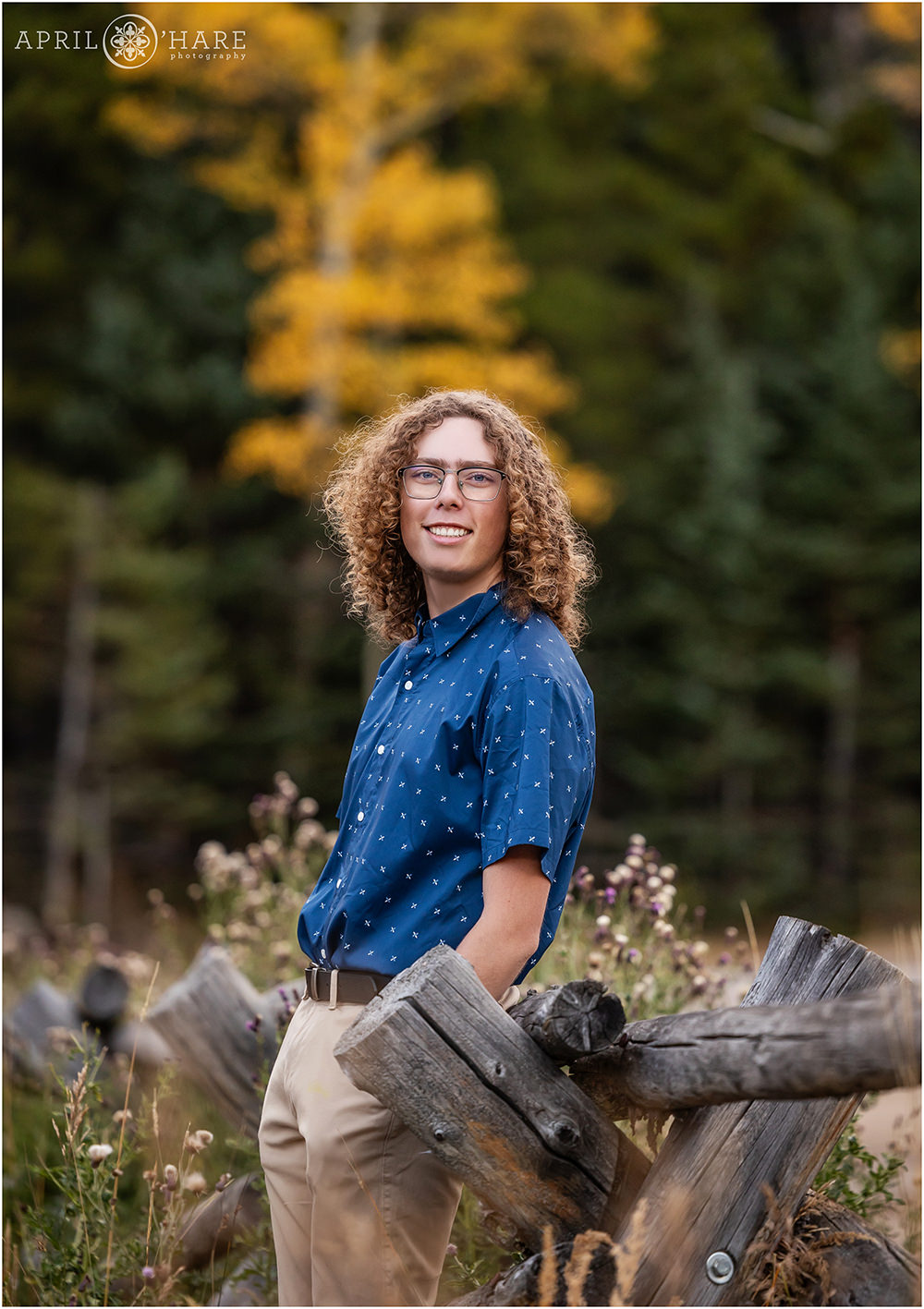 Senior boy with glasses and bright blue short sleeve button down shirt with fall color backdrop in Evergreen, CO