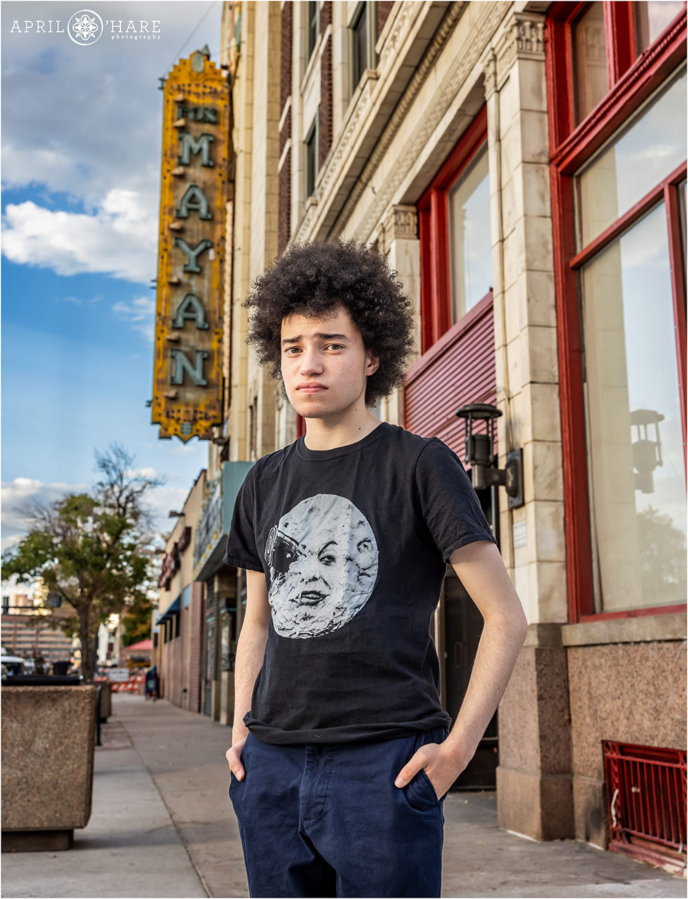 Senior portrait of a teenage boy wearing a Georges Méliès A Trip to the Moon Tshirt in front of the Historic Mayan Theater on South Broadway in Denver
