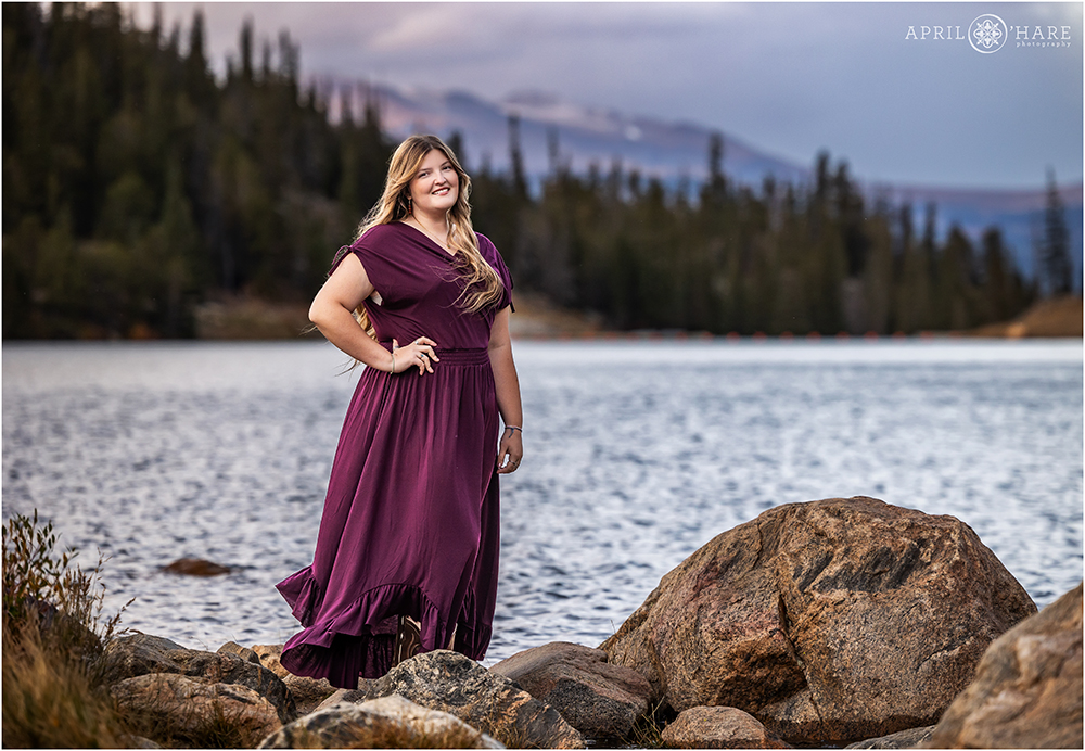 Senior girl wearing a long purple plum colored dress with a lake and mountain backdrop on Guanella Pass in Colorado at Sunset
