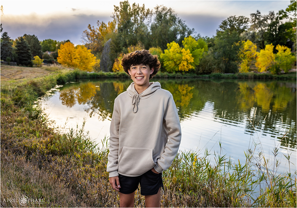 Young teen boy in front of a small pond with fall color backdrop near his home in Littleton CO