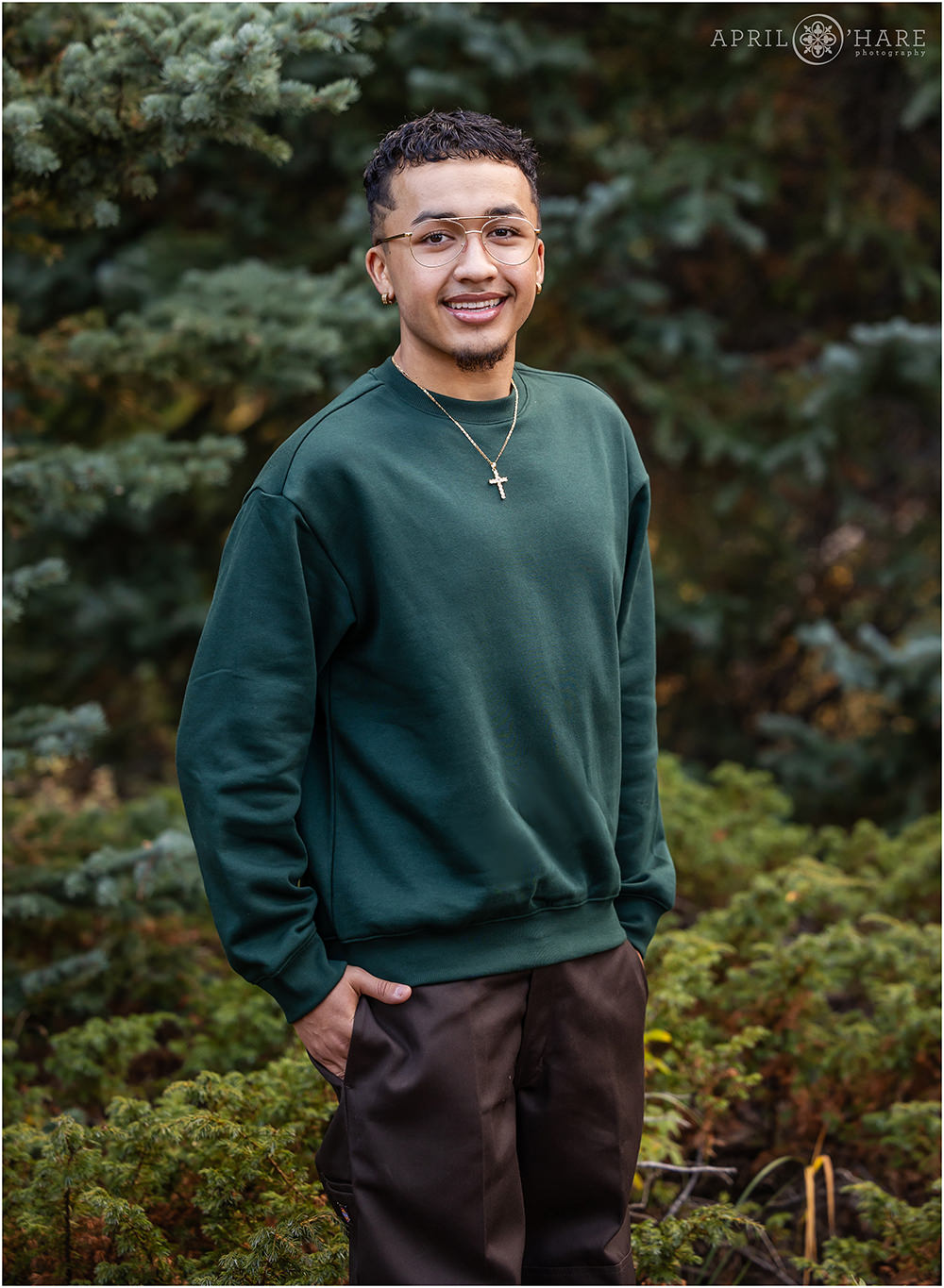 Young man wearing a green sweater stands for a portrait in the woods of Evergreen Colorado