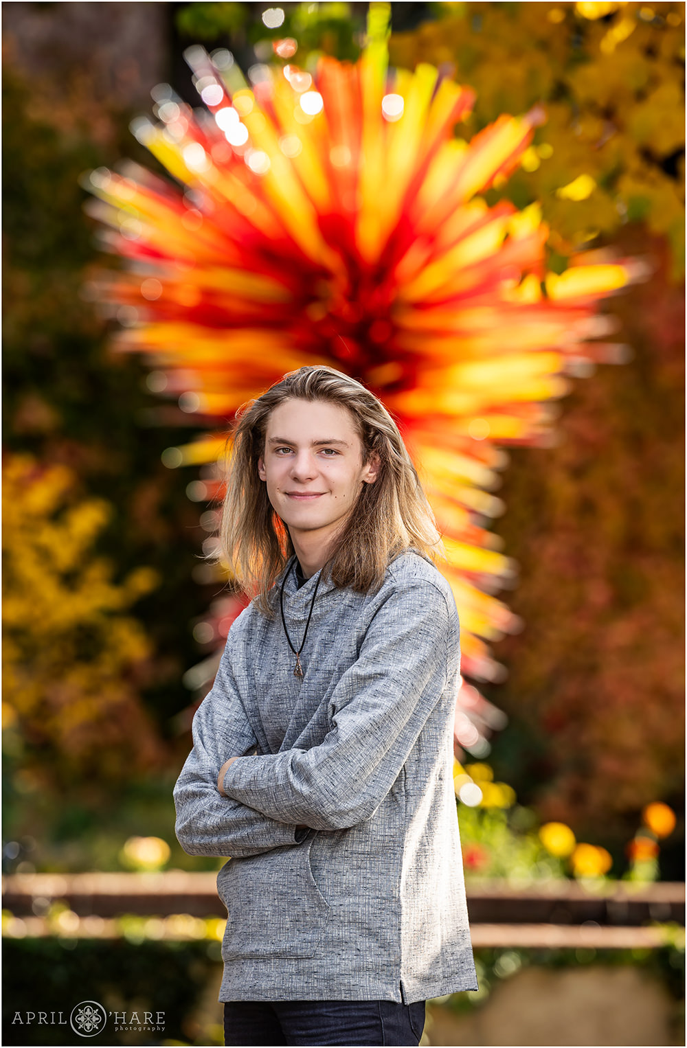 Senior photography with red and yellow Chihuly Sculpture in the backdrop with fall color at an autumn senior photoshoot at Denver Botanic Gardens