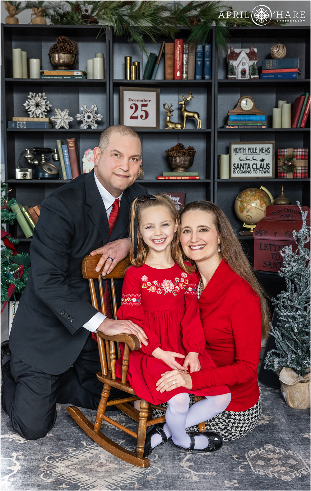 A cute family of 3 pose in a Christmas library setting inside a studio in Denver Colorado