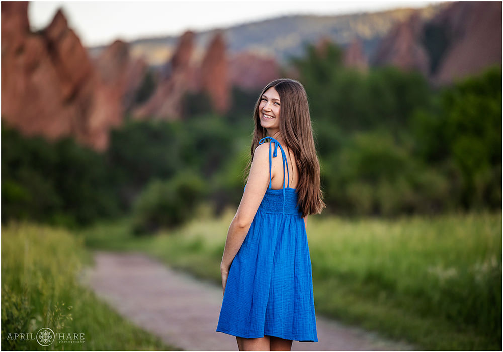 High School Senior Girl wearing a blue sundress walking on the path at Roxborough State Park in Colorado