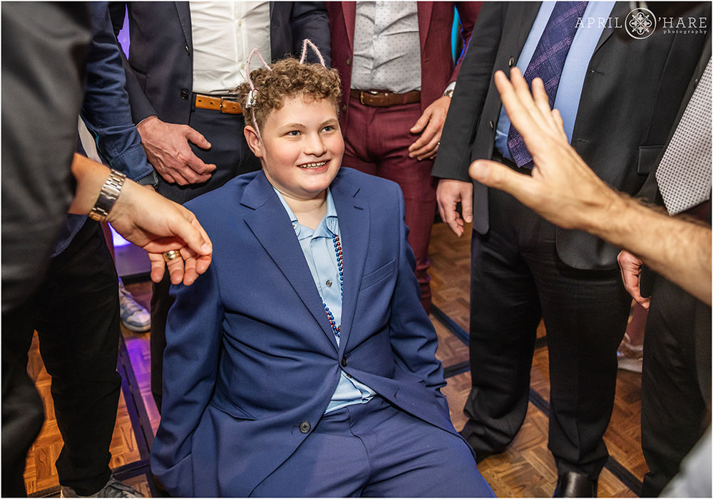 Bar mitzvah boy smiles as he's about to be lifted in a chair at his bar mitzvah party in Denver, CO