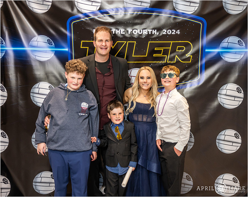 A famioly of 5 with three boys pose for a photo in front of the Star Wars Basketball themed step and repeast backdrop at a bar mitzvah party in Denver