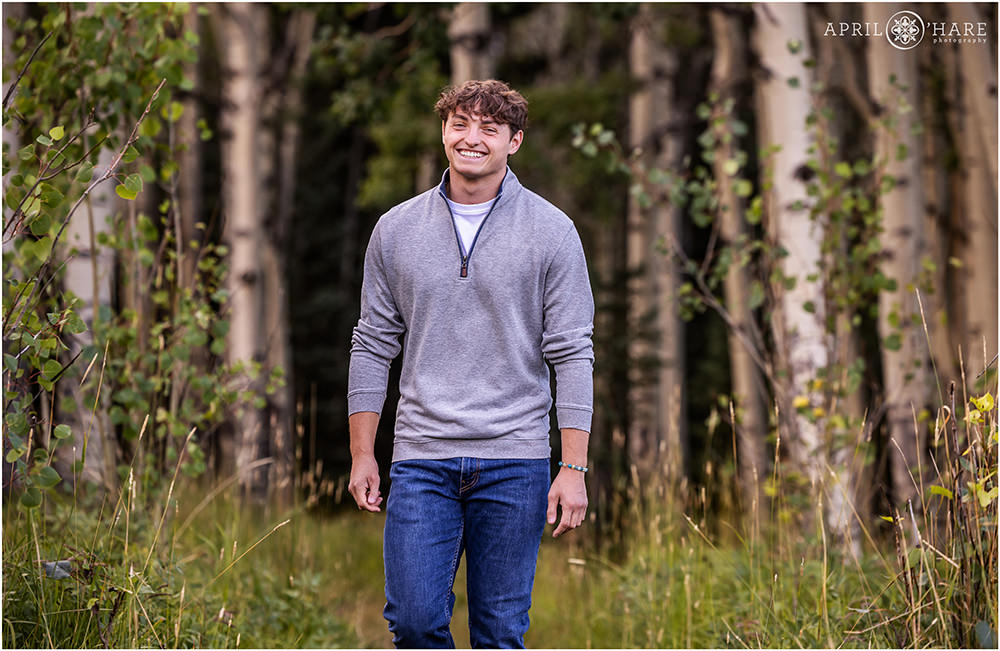 Young Colorado senior walks through an aspen tree forest for his senior photoshoot in Evergreen