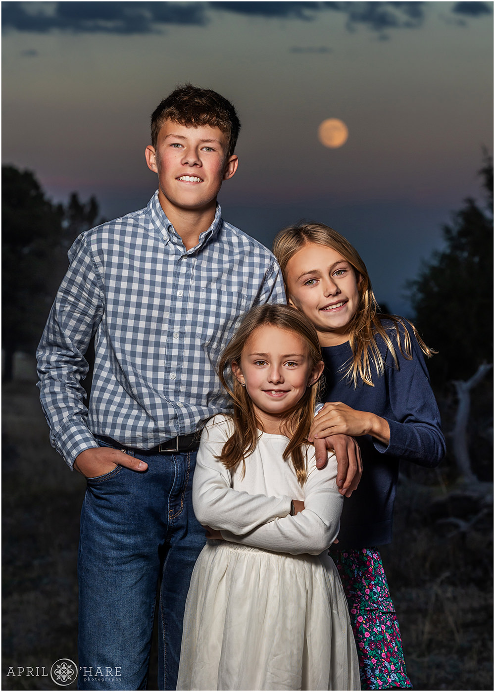 Siblings photo with a full moon backdrop at dusk at West Mount Falcon in Colorado