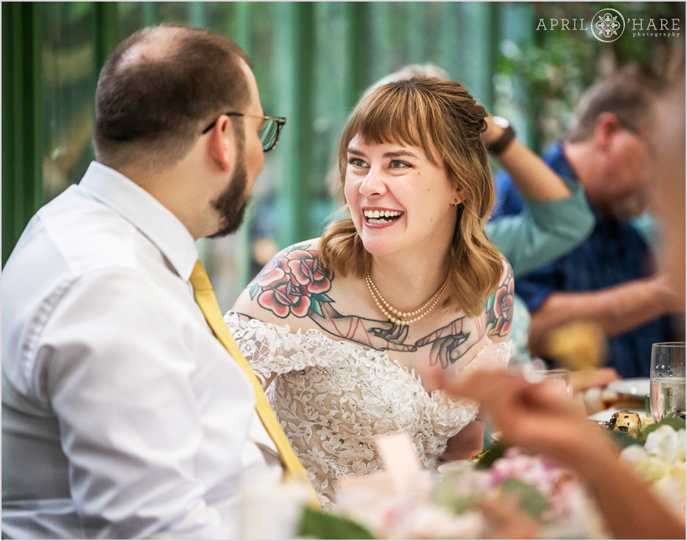 Bride and groom have a moment during their reception dinner to laugh together at Woodland Mosaic Solarium at Denver Botanic Gardens