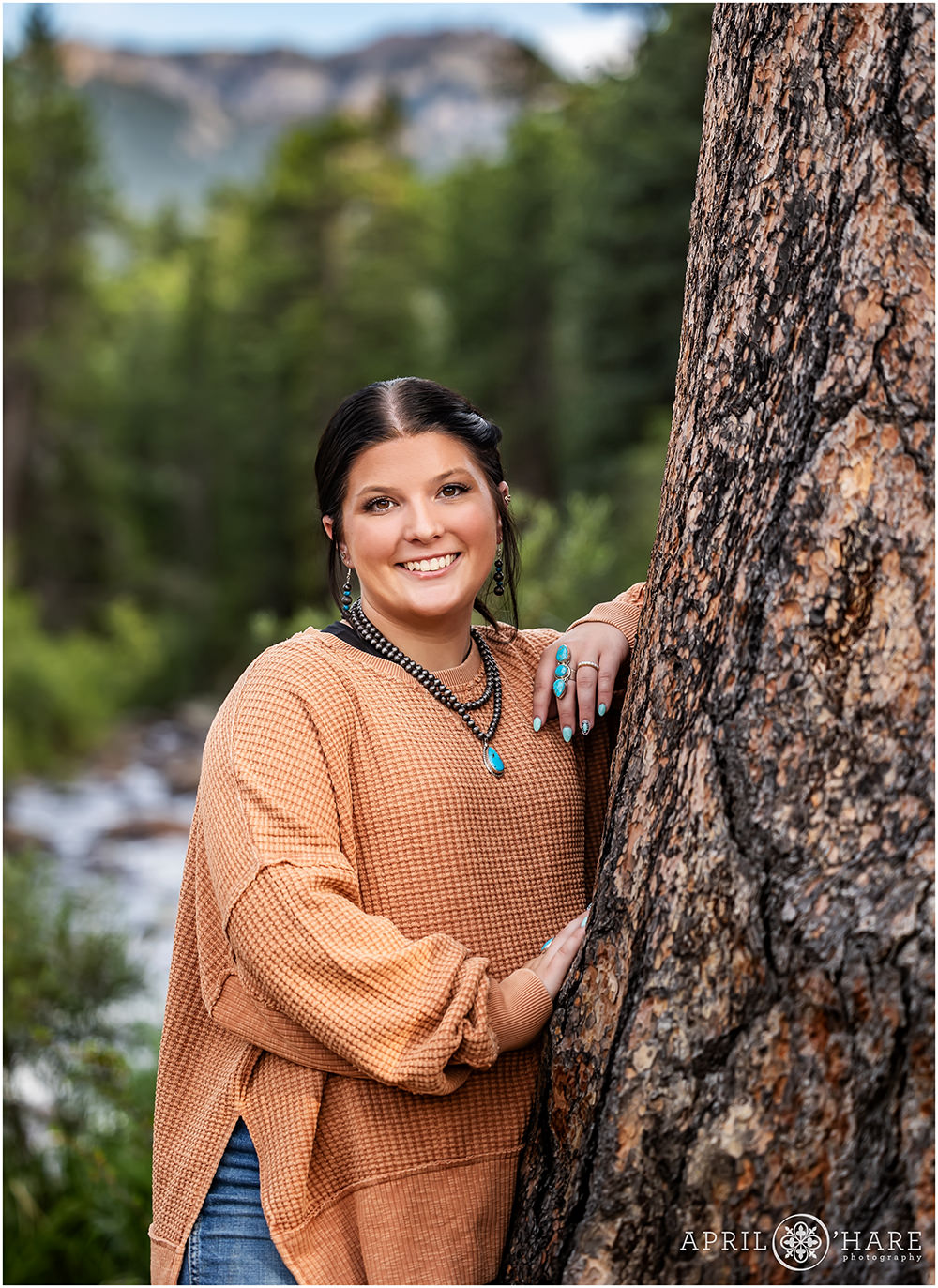 Senior wearing an orange waffle sweater with river backdrop at RMNP in Estes Park