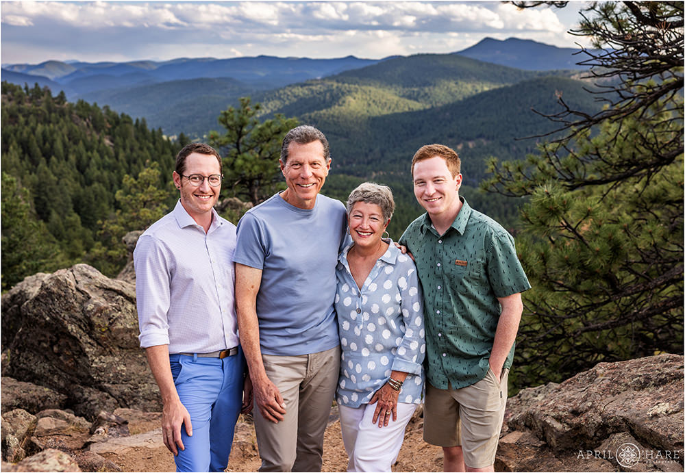 Family of four with two adult sons pose on the rocks with mountain backdrop at West Mount Falcon