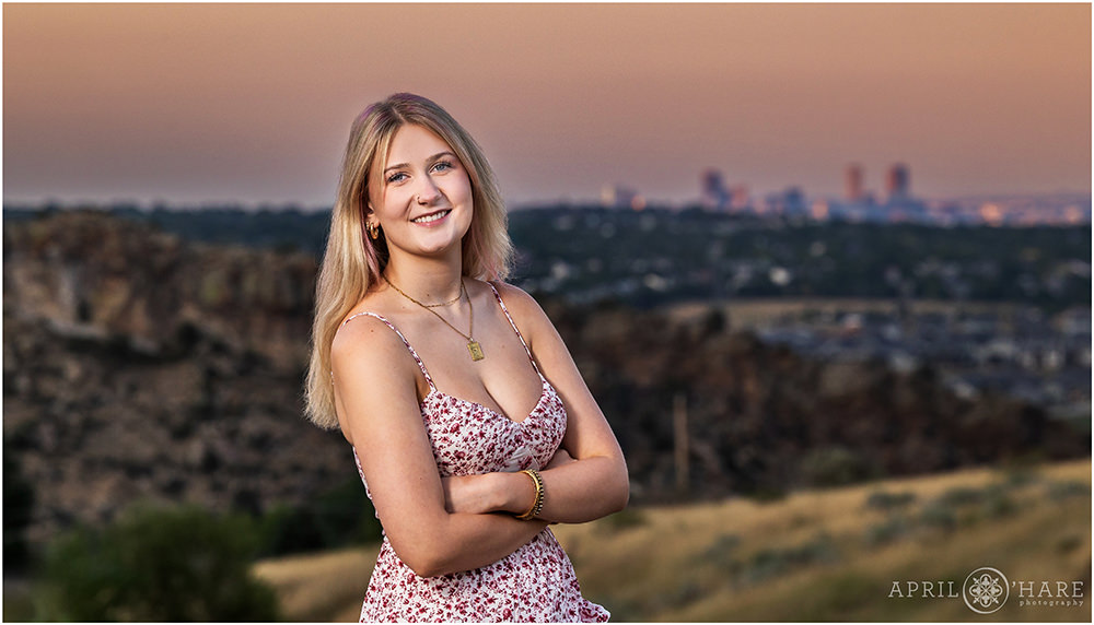 Senior girl with City of Denver Skyline in the distance at Morrison Trailhead at sunset in Colorado