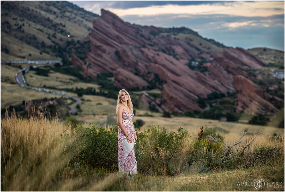 Senior photo at sunset with Red Rocks Ampitheater off in the distance behind her at the Morrison Trailhead