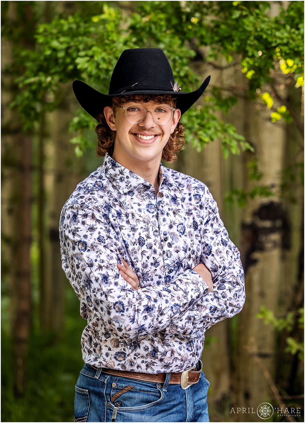 Senior boy poses for a portrait with his black cowboy hat in front of a nice grove of aspen trees in Summit County Colorado