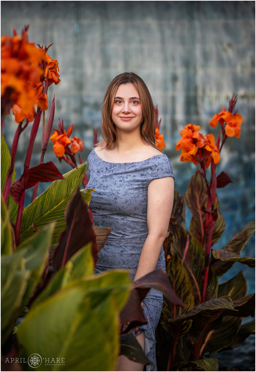 Stunning photo of a senior standing in front of a blue fountain with Orange flowers framing her at Denver Botanic Gardens