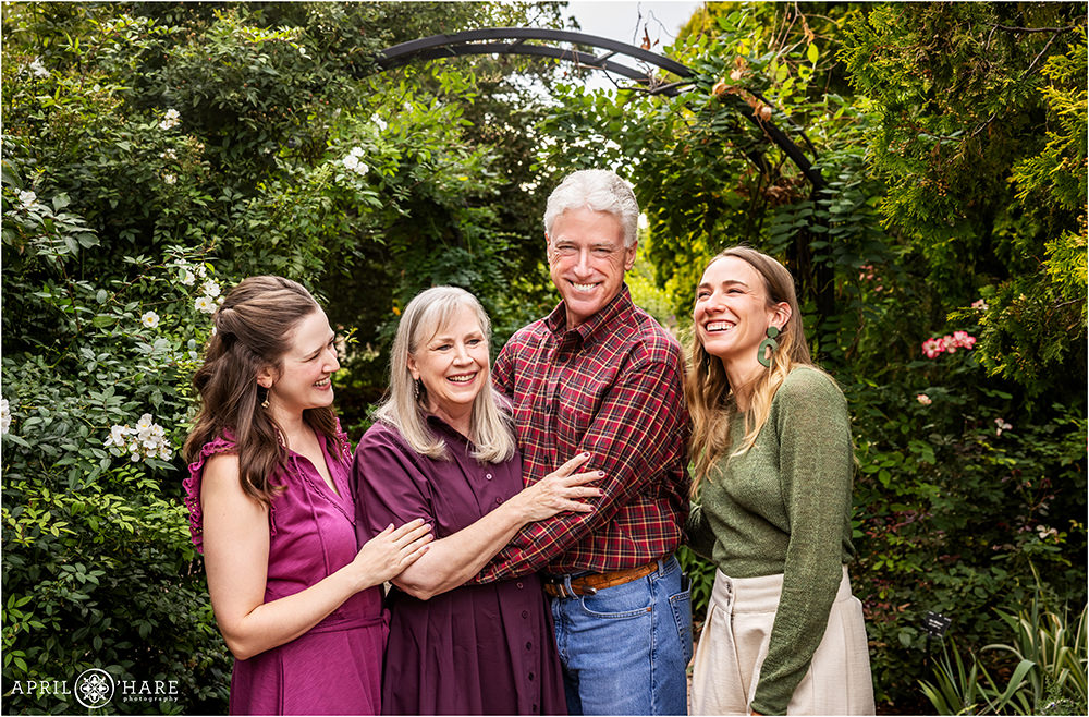 Family of four with two adult daughters laugh together for a candid photo at Denver Botanic Gardens