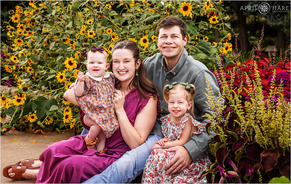 Cute family photo with two young daughters sit on the ground surrounded by flowers at Denver Botanic Gardens