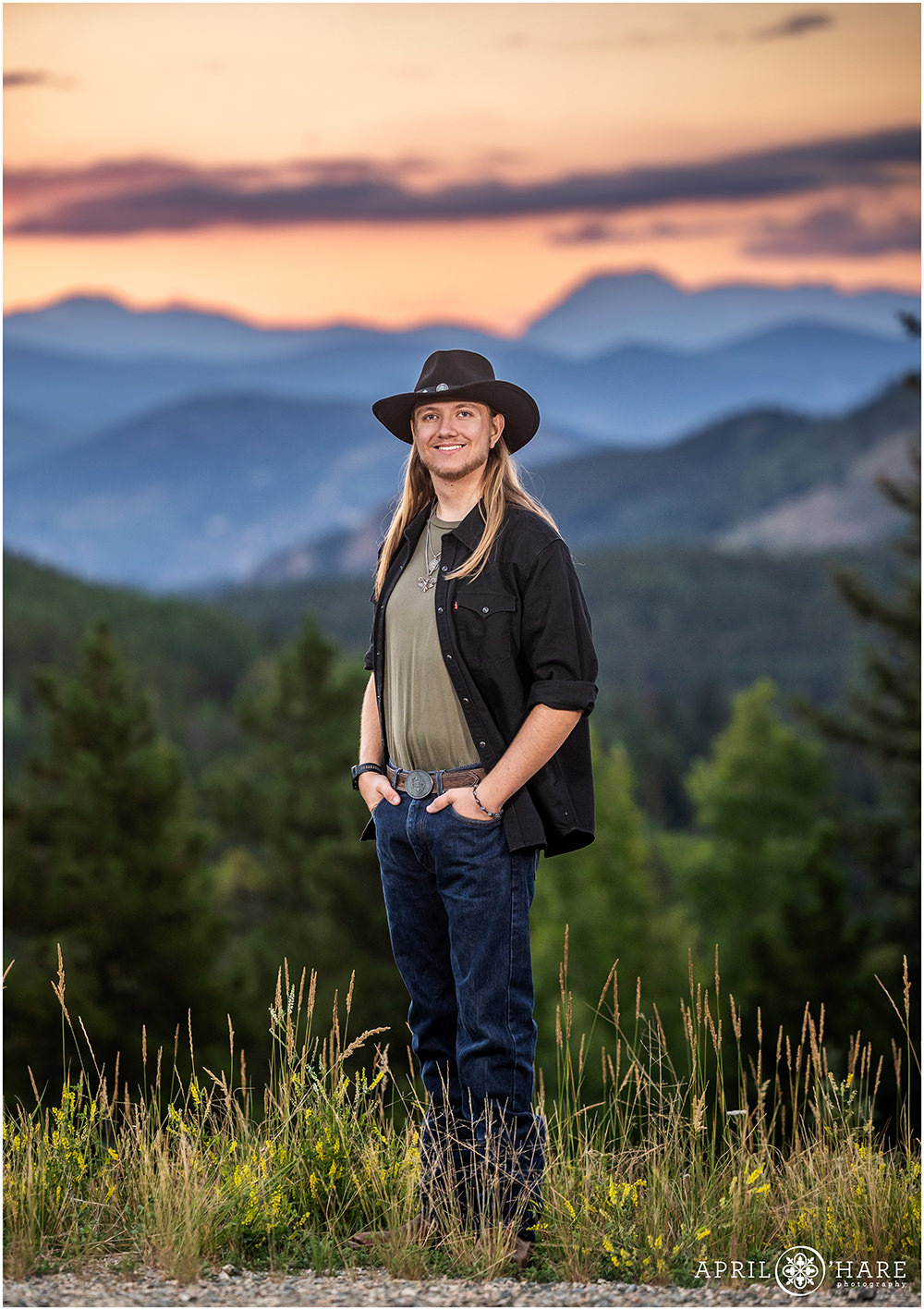 Senior boy wearing a black hat poses with a mountain backdrop on Squaw Pass Road in Colorado