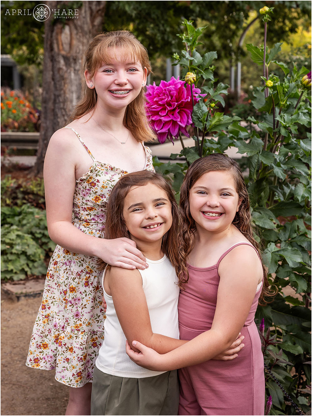 Three sisters pose with a huge pretty dinnerplate Dahlia at Denver Botanic Gardens