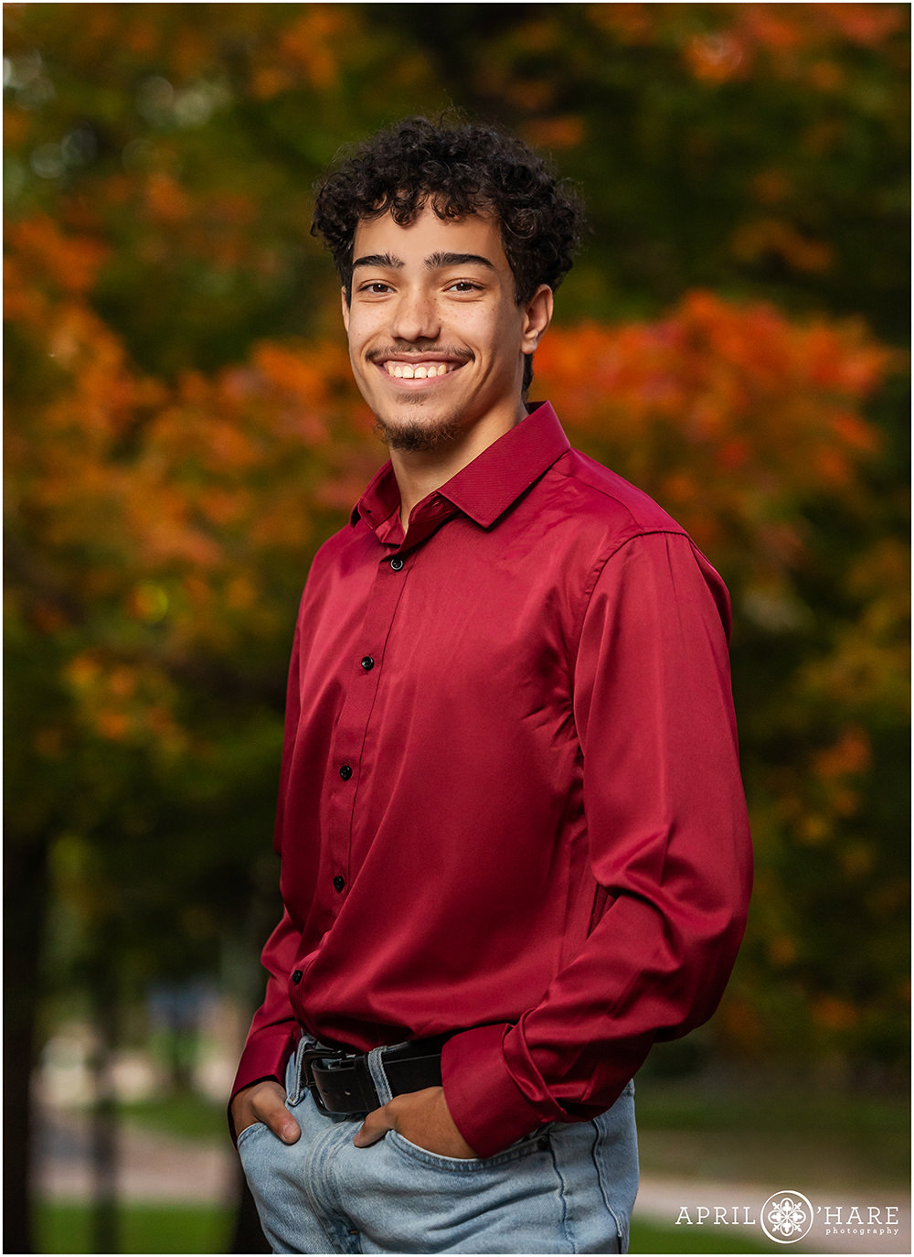 High school senior portrait for a young man wearing a red button down shirt with a pretty fall color leaves backdrop