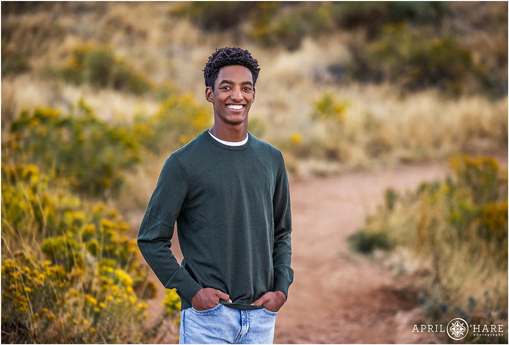 High school senior boy wearing a green long sleeved shirt in the beautiful yellow fall color along the trail at Morrison Trailhead in Colorado