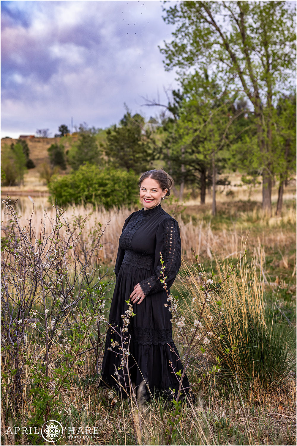 A regal full length style portrait of a woman wearing a long Victorian style black dress in the spring blossoms at Viele Lake in Boulder Colorado