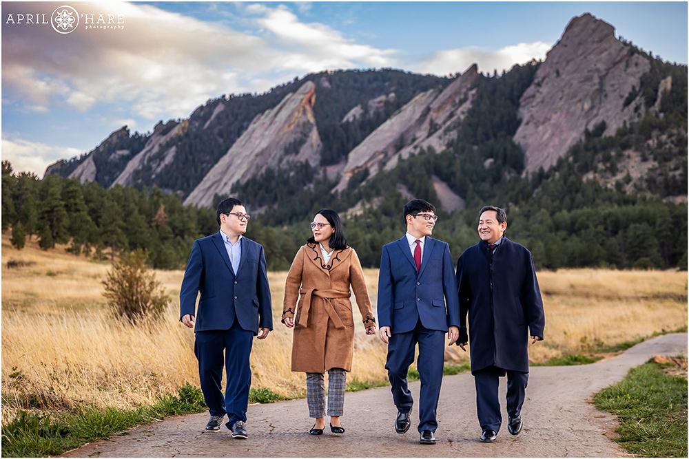 Family of four walk along the path at Chautauqua at their youngest son's college graduation photoshoot with the Flatirons in the backdrop
